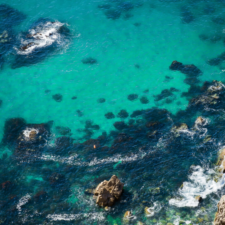 Aerial view of clear turquoise ocean water with scattered rocks and gentle waves.